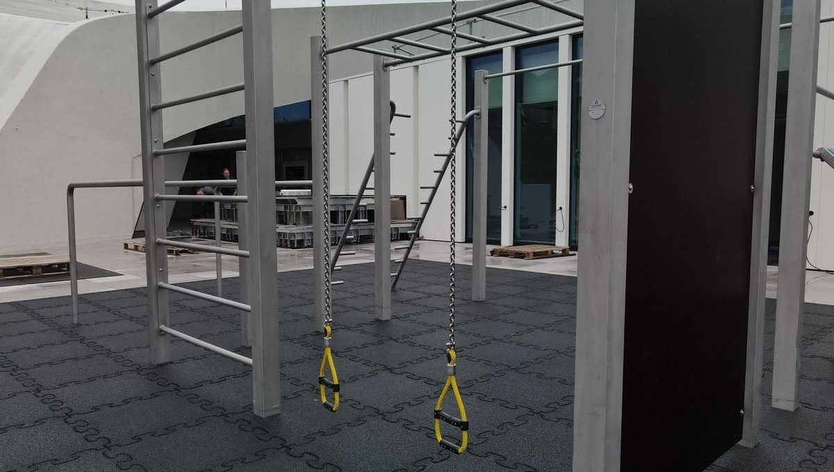 Calisthenics-Anlage mit grauem Fallschutz bei Sonnenschein