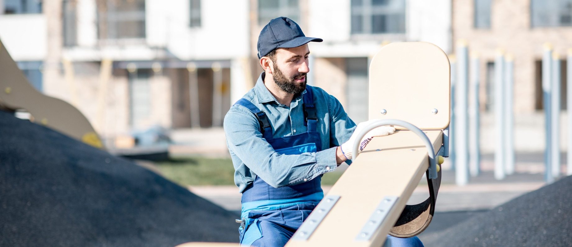 Ein Arbeiter begutachtet die Abnutzung der Wippe auf dem Spielplatz